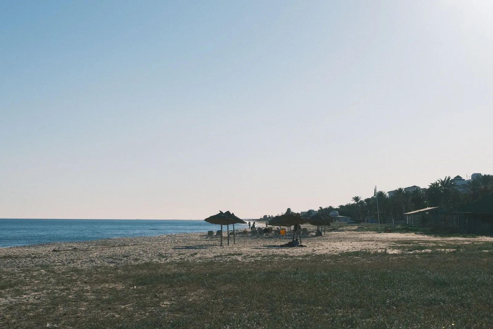 Plage tunisienne déserte avec un parasol de paille sous un ciel voilé