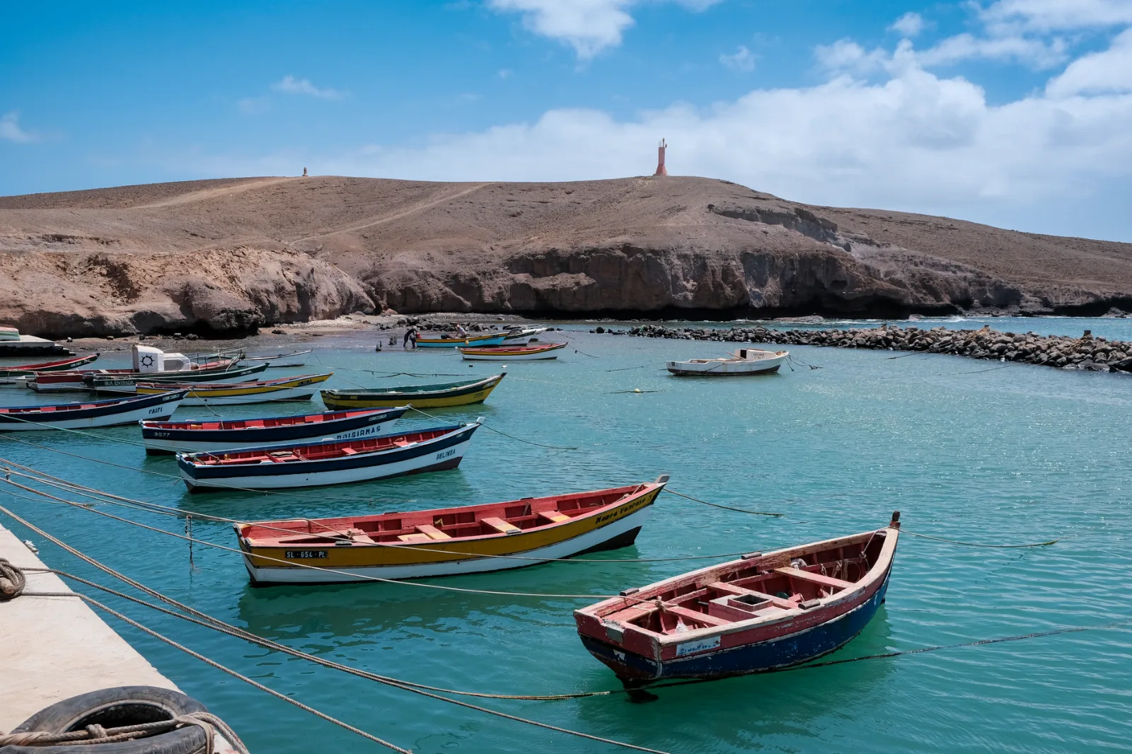 Barques de pêche colorées amarrées dans la baie turquoise de Pedra Lume, devant une colline dénudée