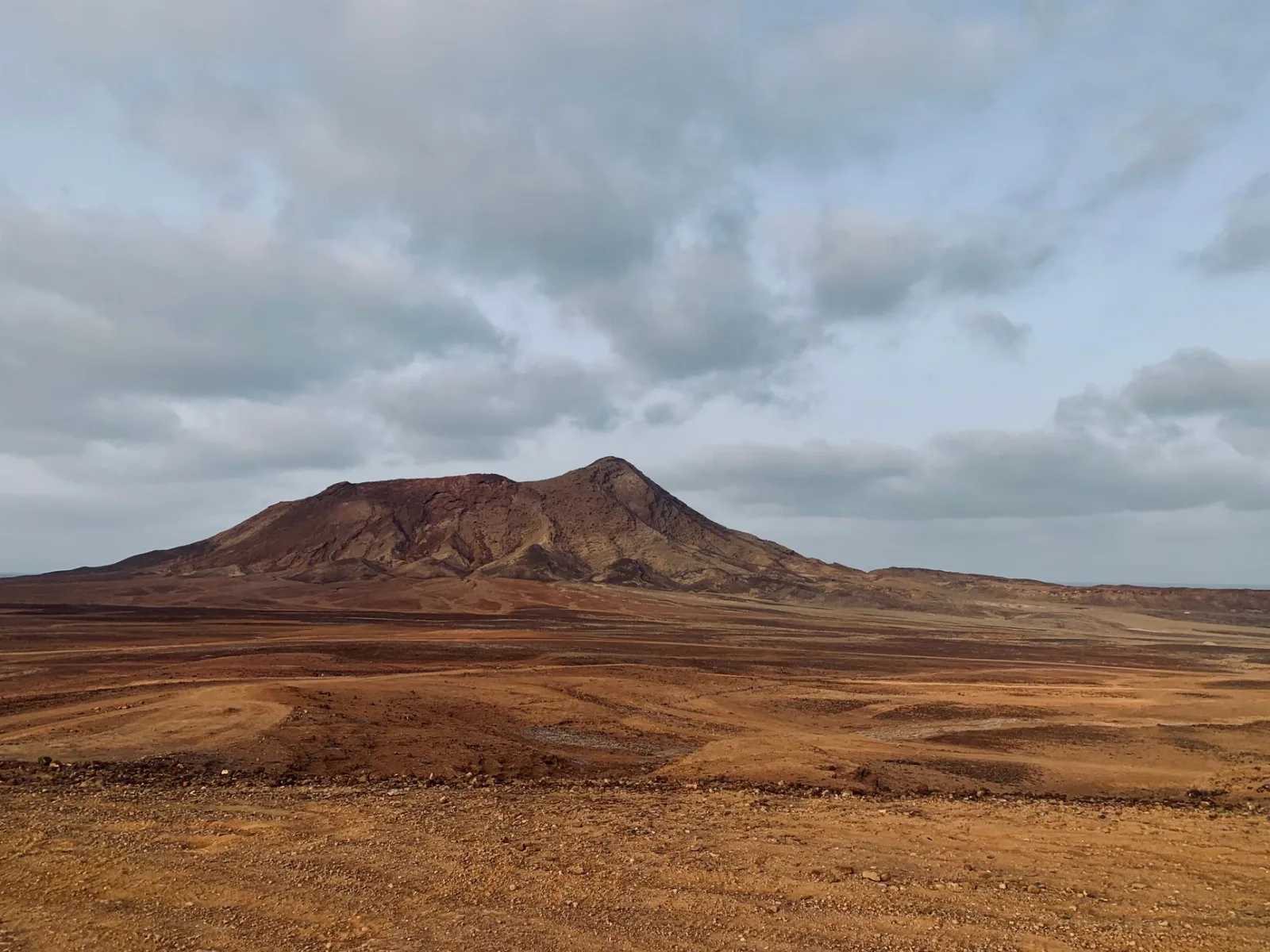 Plaine brune et aride de l'île de Sal, au Cap-Vert, dominée par un cône volcanique sous un ciel voilé