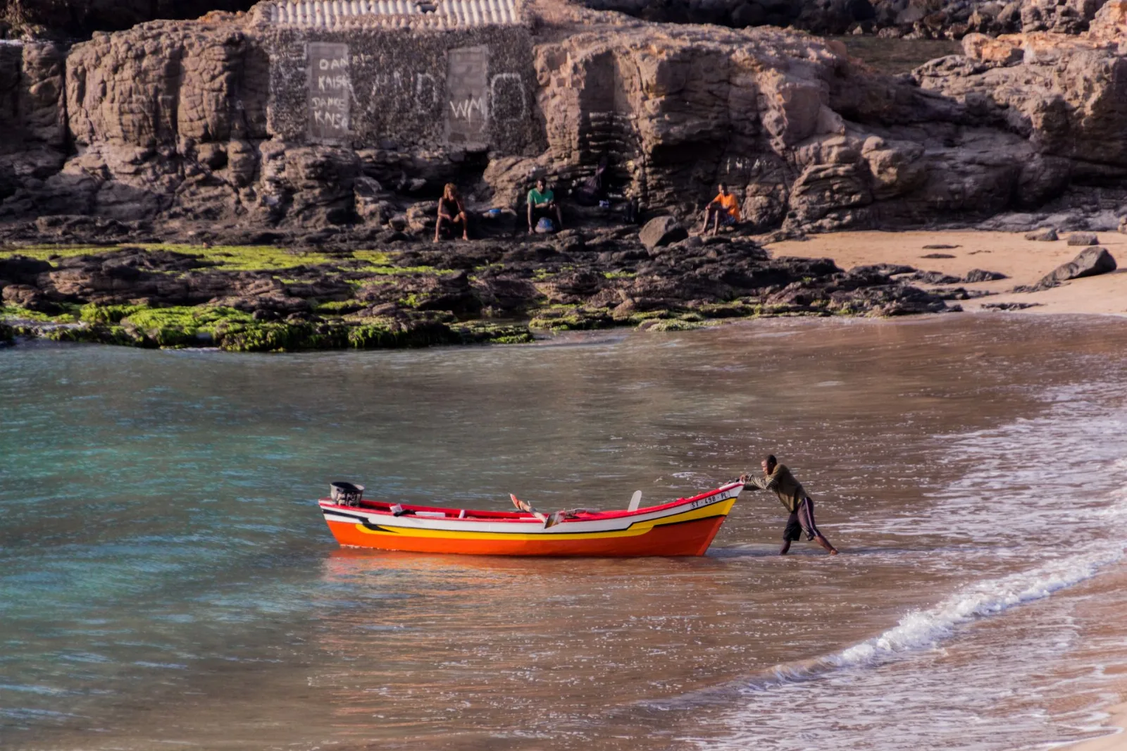 Barque de pêche rouge et jaune poussée vers le rivage sur la plage de Tarrafal, au Cap-Vert