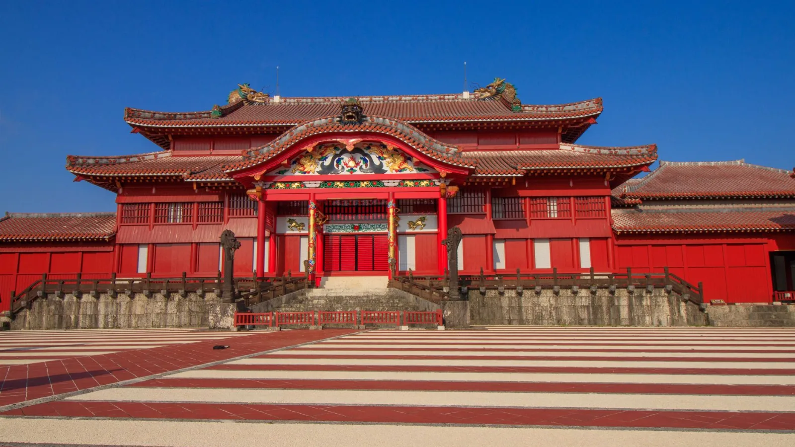 Façade vermillon du château de Shuri à Okinawa sous un ciel bleu, escalier de pierre claire