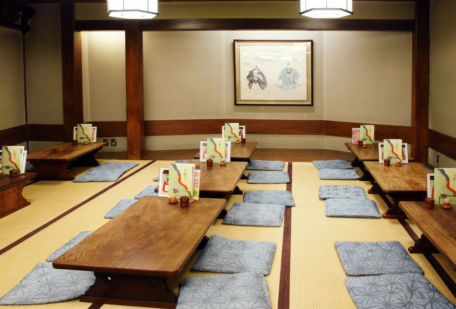 Salle de ryokan avec tables basses en bois alignées sur tatami et coussins gris