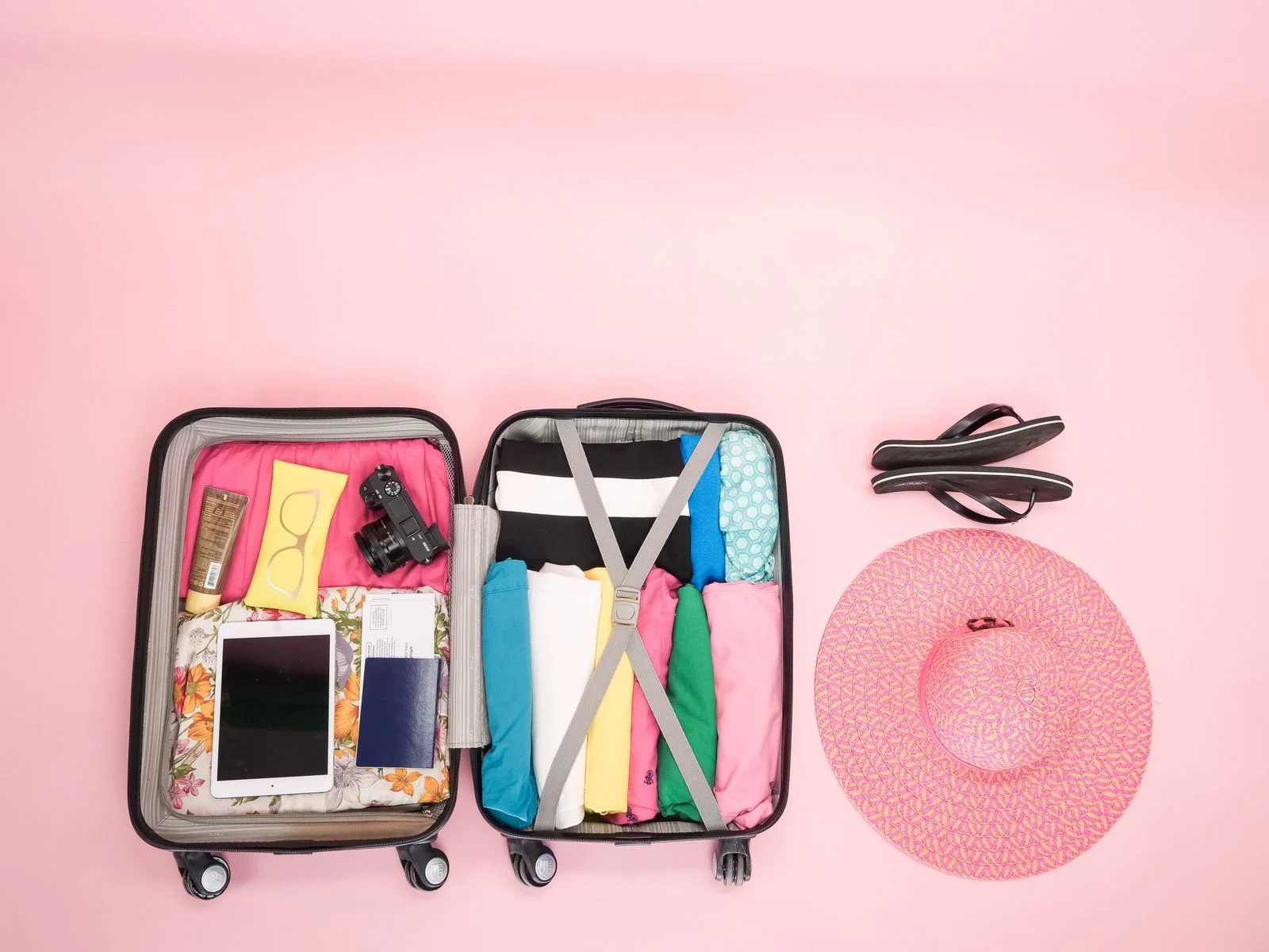 Valise ouverte vue de dessus avec vêtements pliés, chapeau et tongs