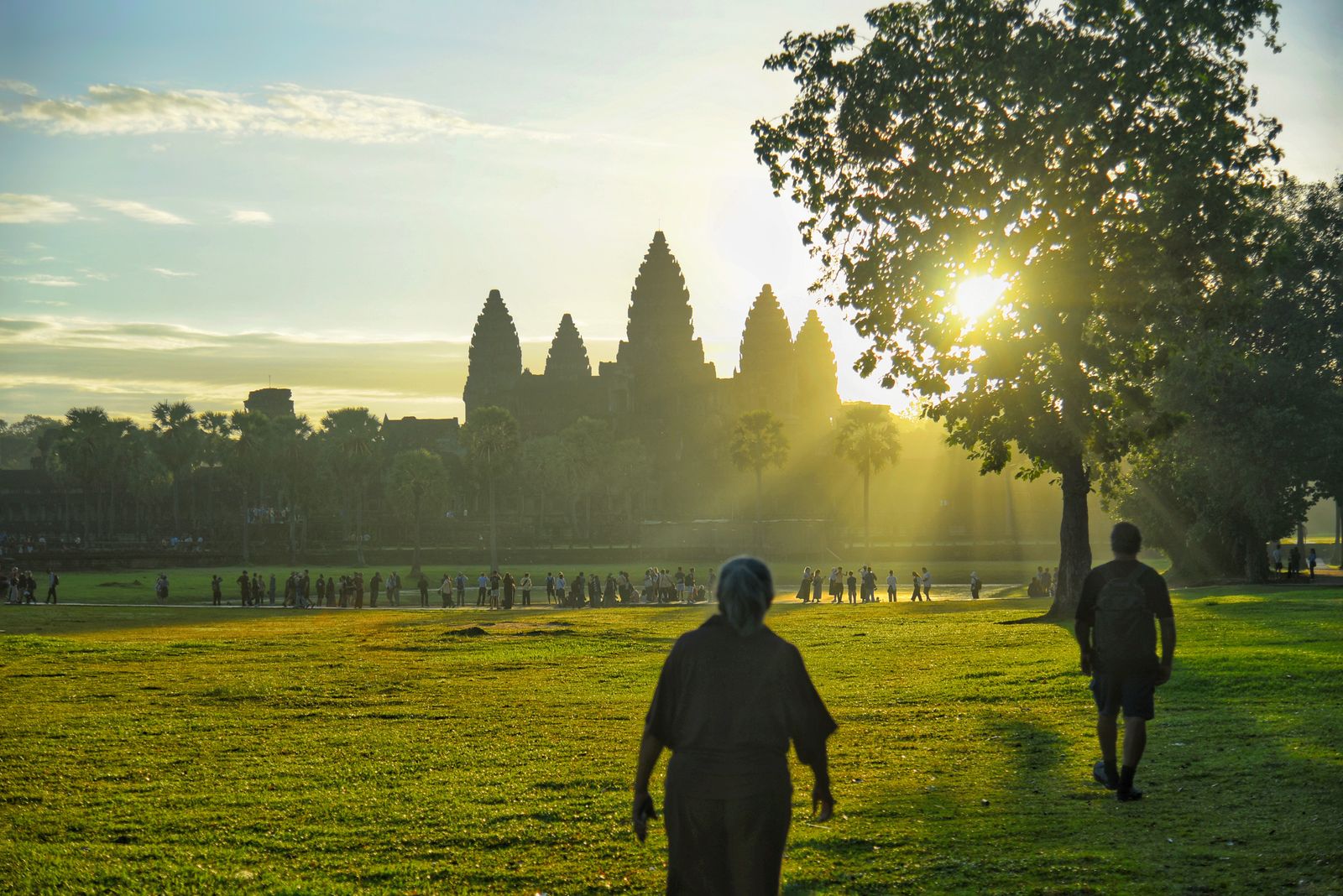 Visiteurs marchant sur la pelouse vers les tours d'Angkor Wat, à contre-jour au lever du soleil