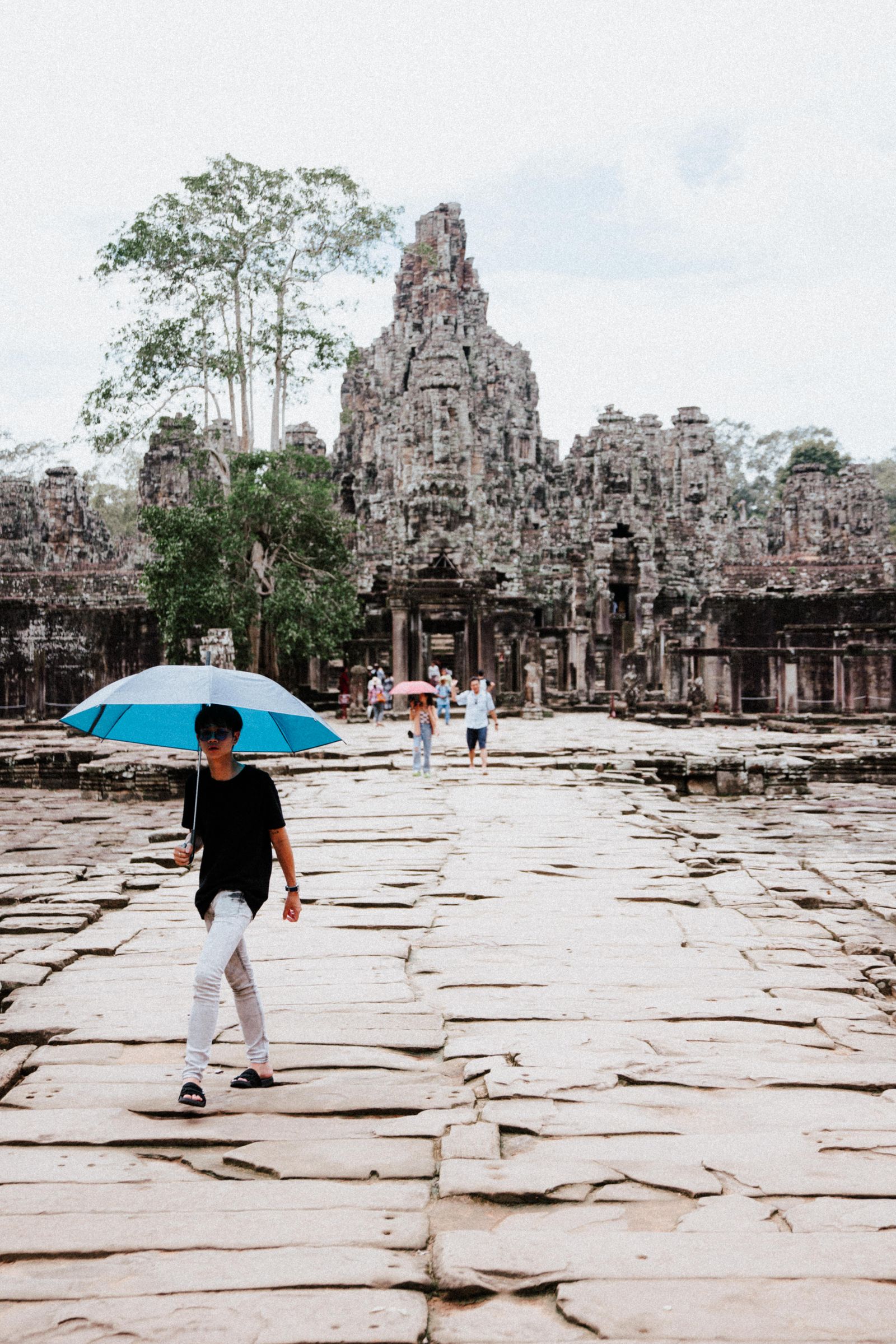 Visiteur abrité sous un parapluie bleu sur la chaussée du Bayon, devant les tours à visages