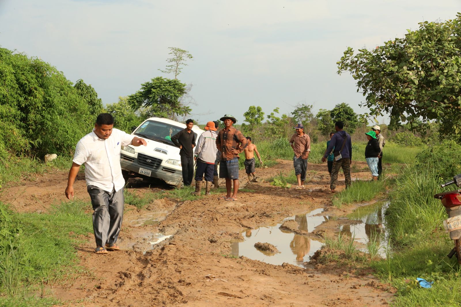 Piste de terre détrempée au Mondulkiri, avec un pick-up embourbé et des marcheurs dans la boue
