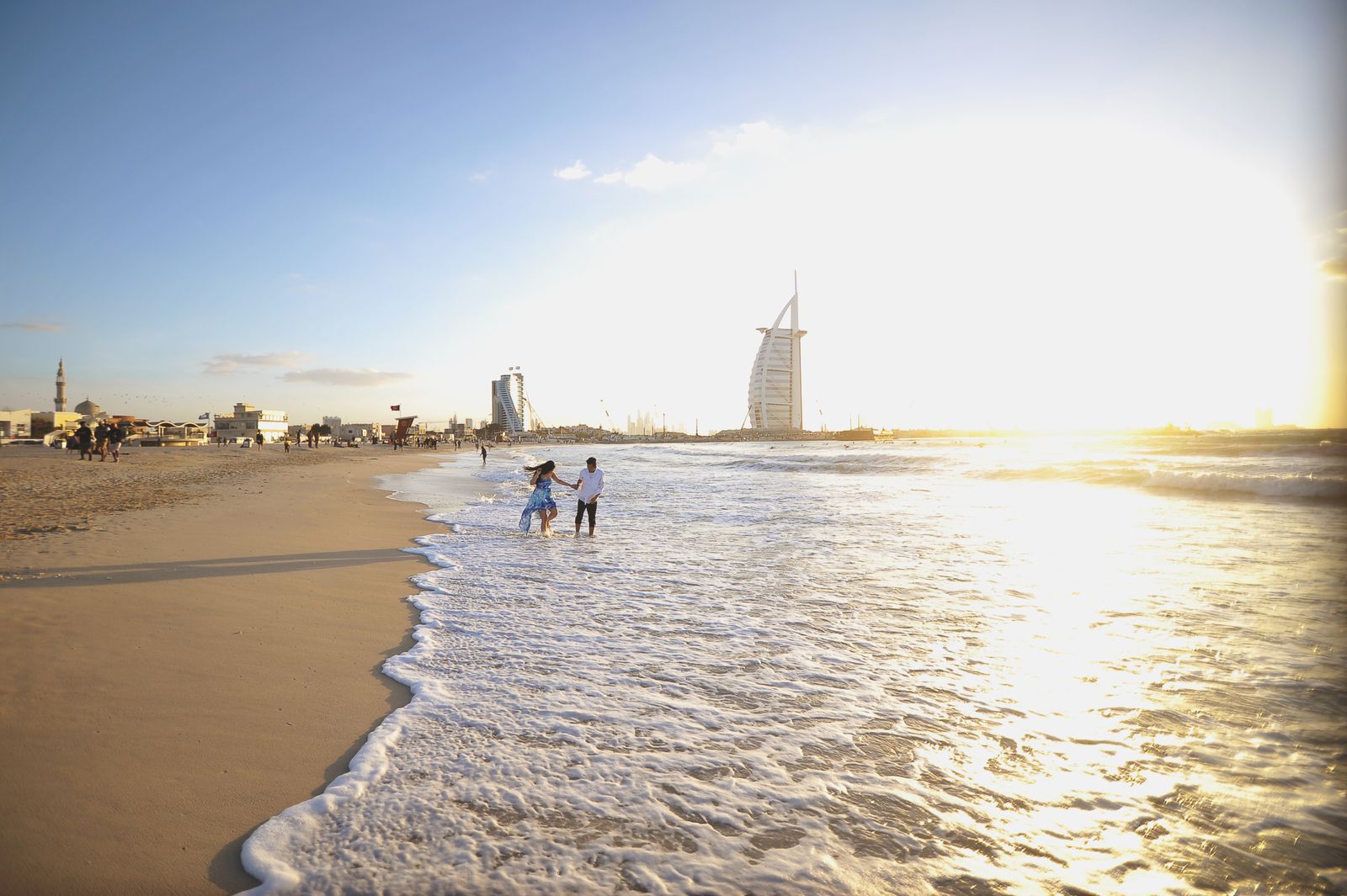 Plage de Jumeirah au coucher du soleil, promeneurs au bord de l'eau et Burj Al Arab à l'horizon