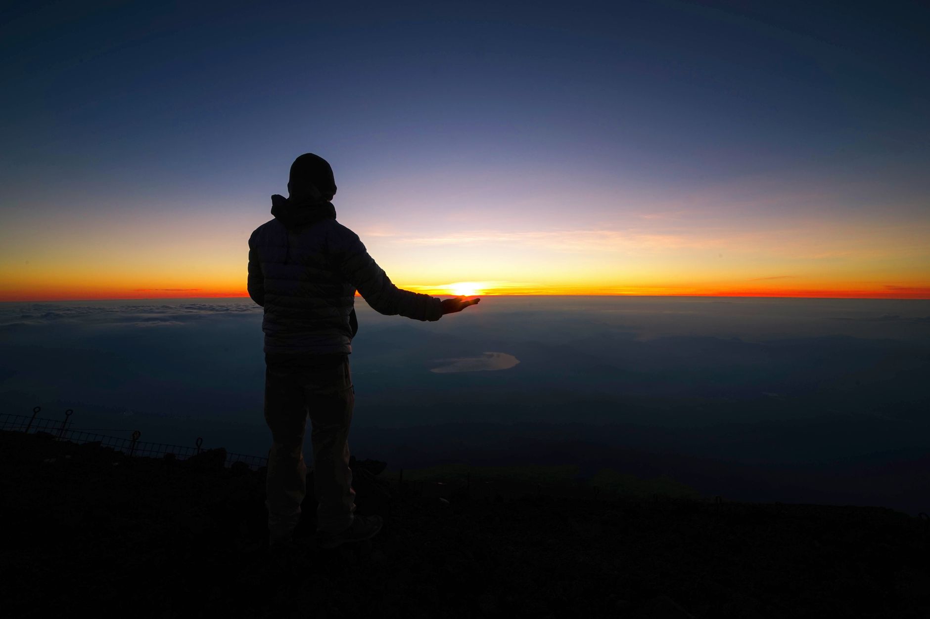 Un randonneur face au lever du soleil au sommet du mont Fuji, au-dessus d'une mer de nuages