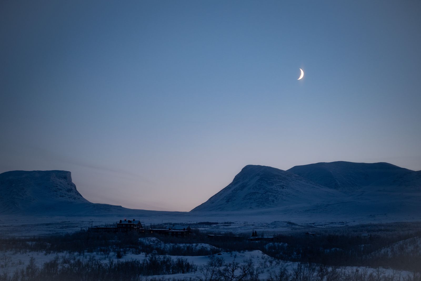 Vallée en U et sommets enneigés à Abisko au crépuscule, sous un croissant de lune