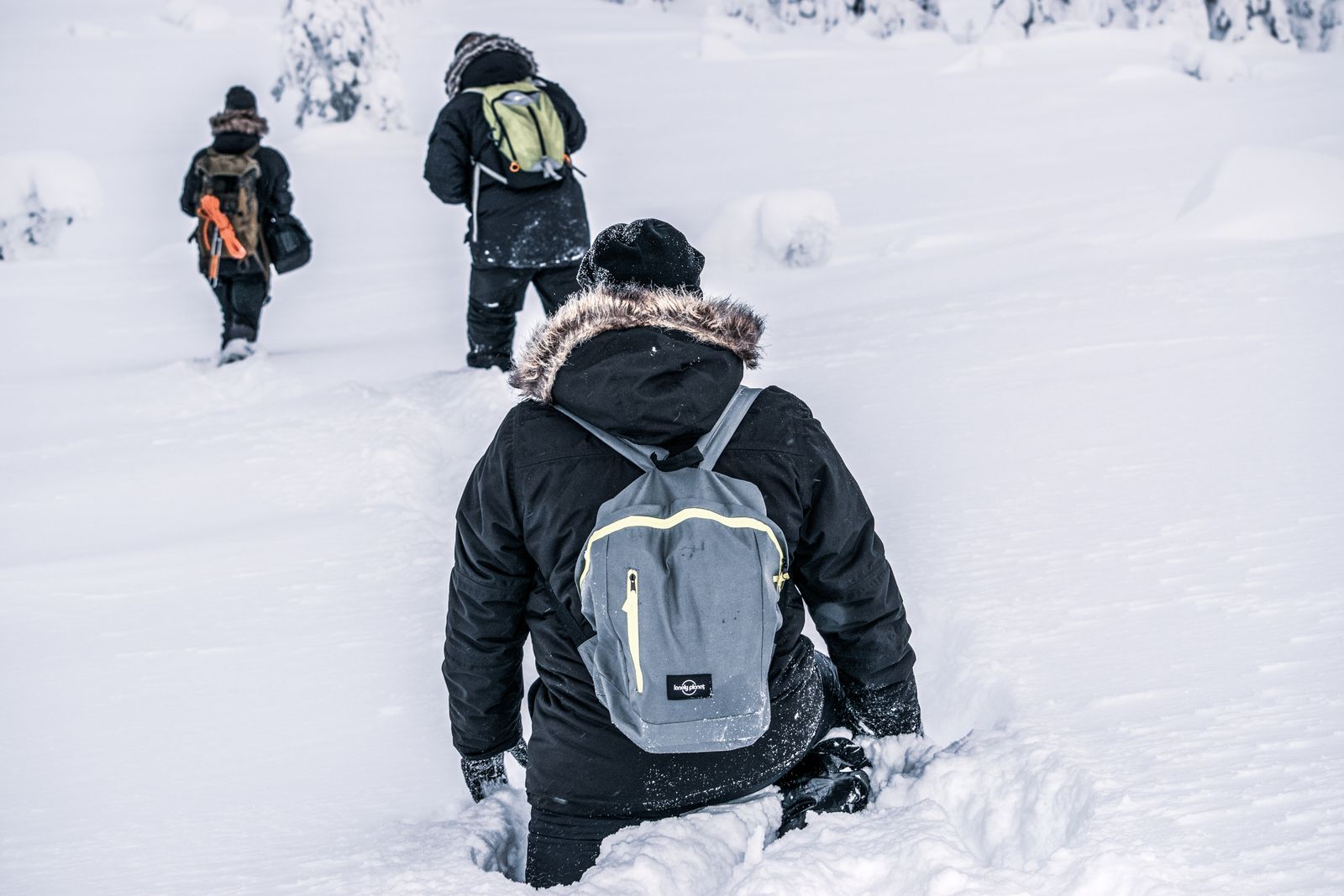 Trois marcheurs de dos dans la neige profonde en Laponie finlandaise, l'un en parka à capuche bordée de fourrure