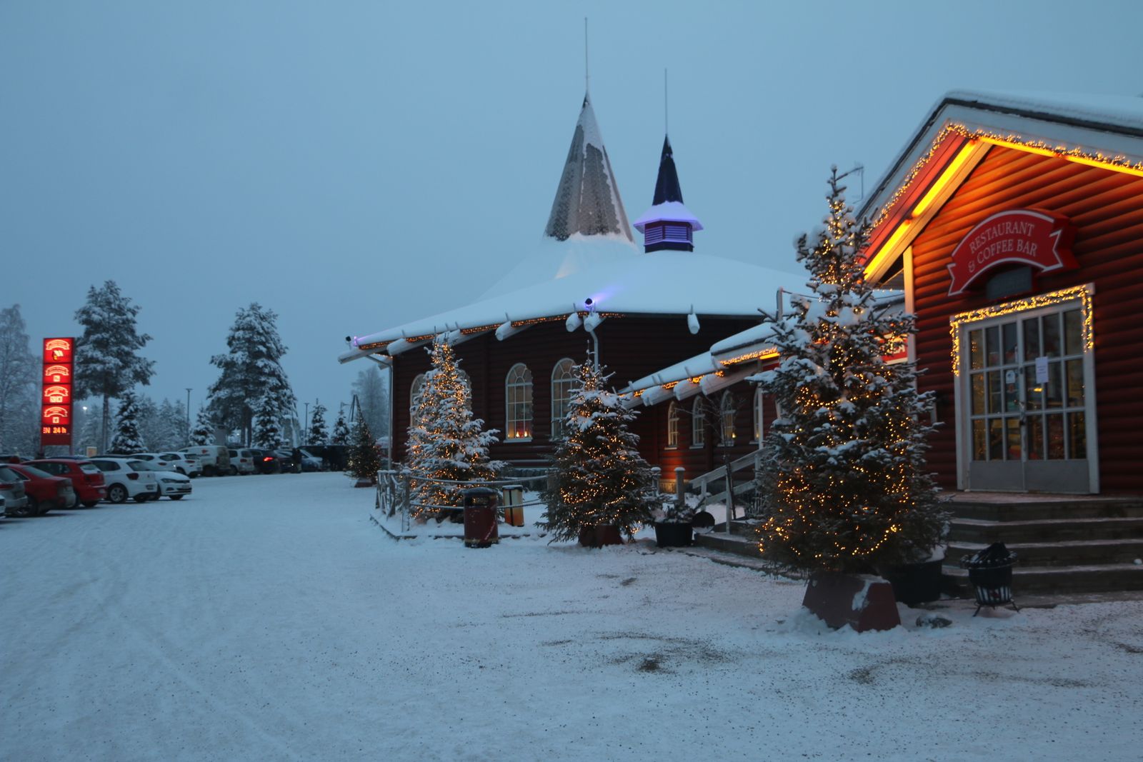 Bâtiments en bois illuminés du village du Père Noël à Rovaniemi, sous la neige au crépuscule