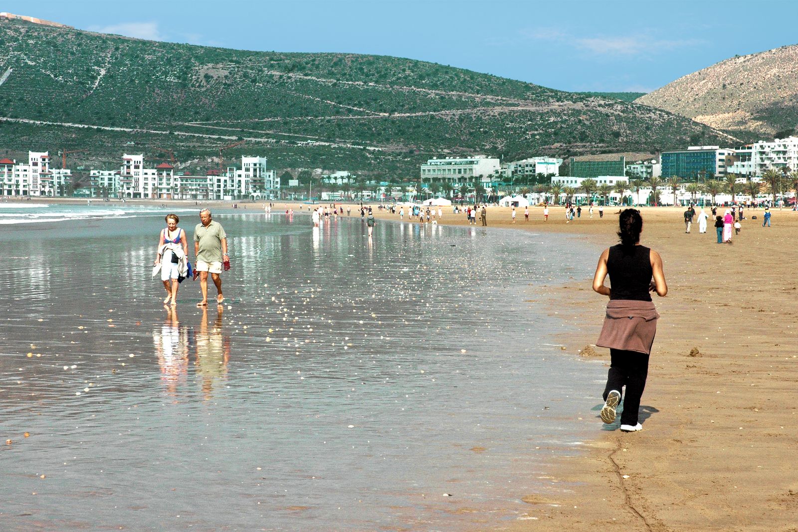 Promeneurs au bord de l'eau sur la plage d'Agadir, devant la baie et ses immeubles