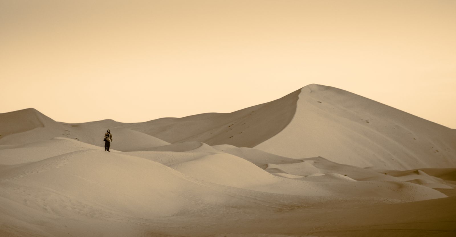 Un marcheur seul sur une dune de l'erg Chebbi, sous un ciel voilé