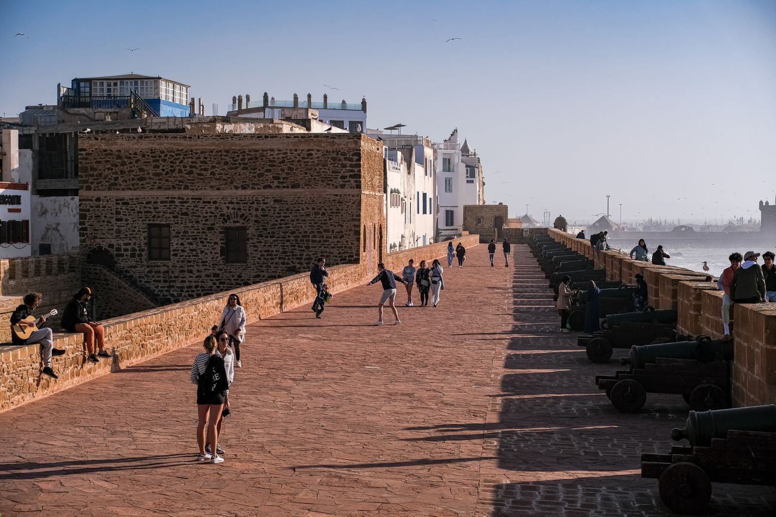 Promeneurs sur les remparts d'Essaouira, le long d'une rangée de canons face à l'océan