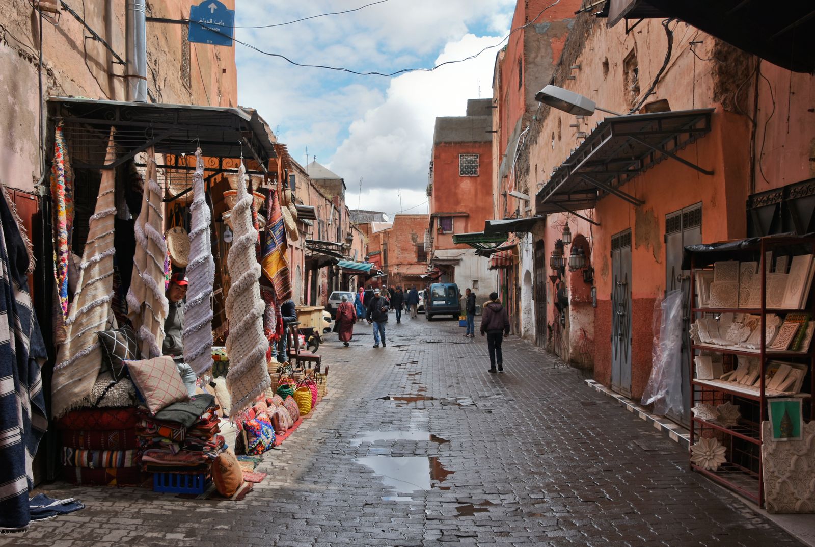 Ruelle pavée et mouillée de la médina de Marrakech, tapis suspendus devant les échoppes