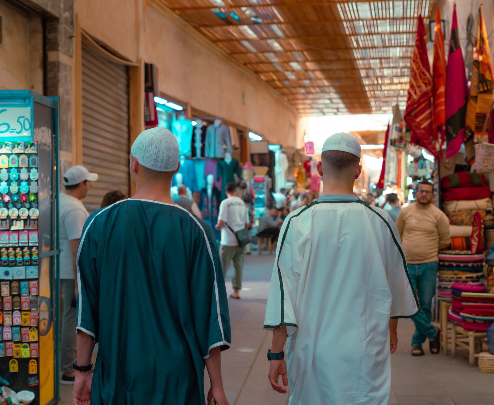 Deux hommes de dos en tunique longue et calotte dans une allée couverte d'un souk de Marrakech