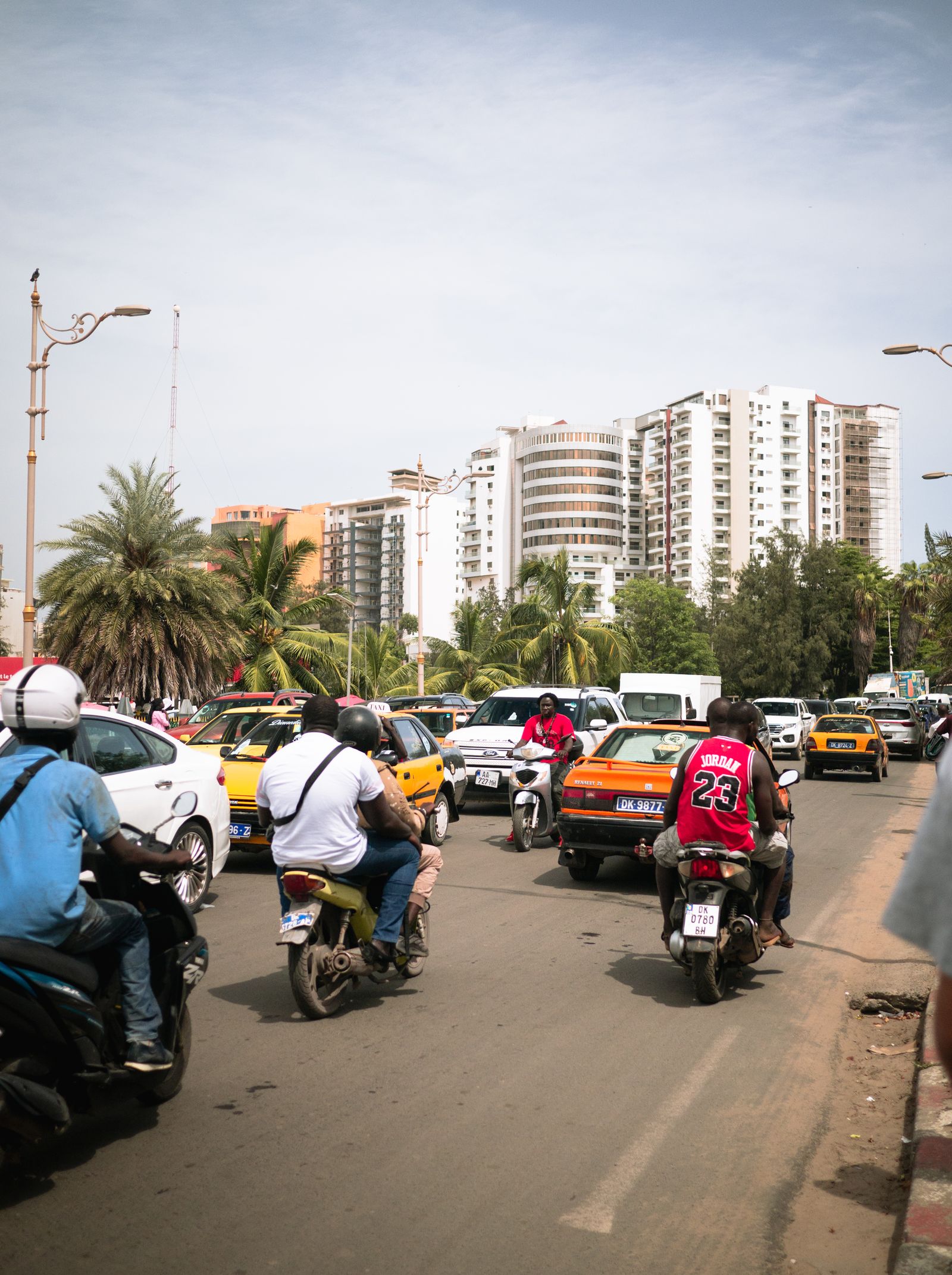 Motos, voitures et taxis jaunes dans une rue de Dakar, avec des immeubles en construction au fond