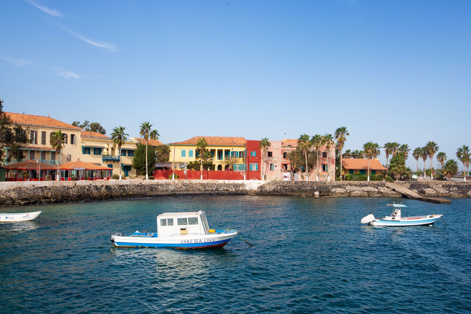 Maisons colorées de l'île de Gorée au bord de l'eau, avec des bateaux à moteur au premier plan