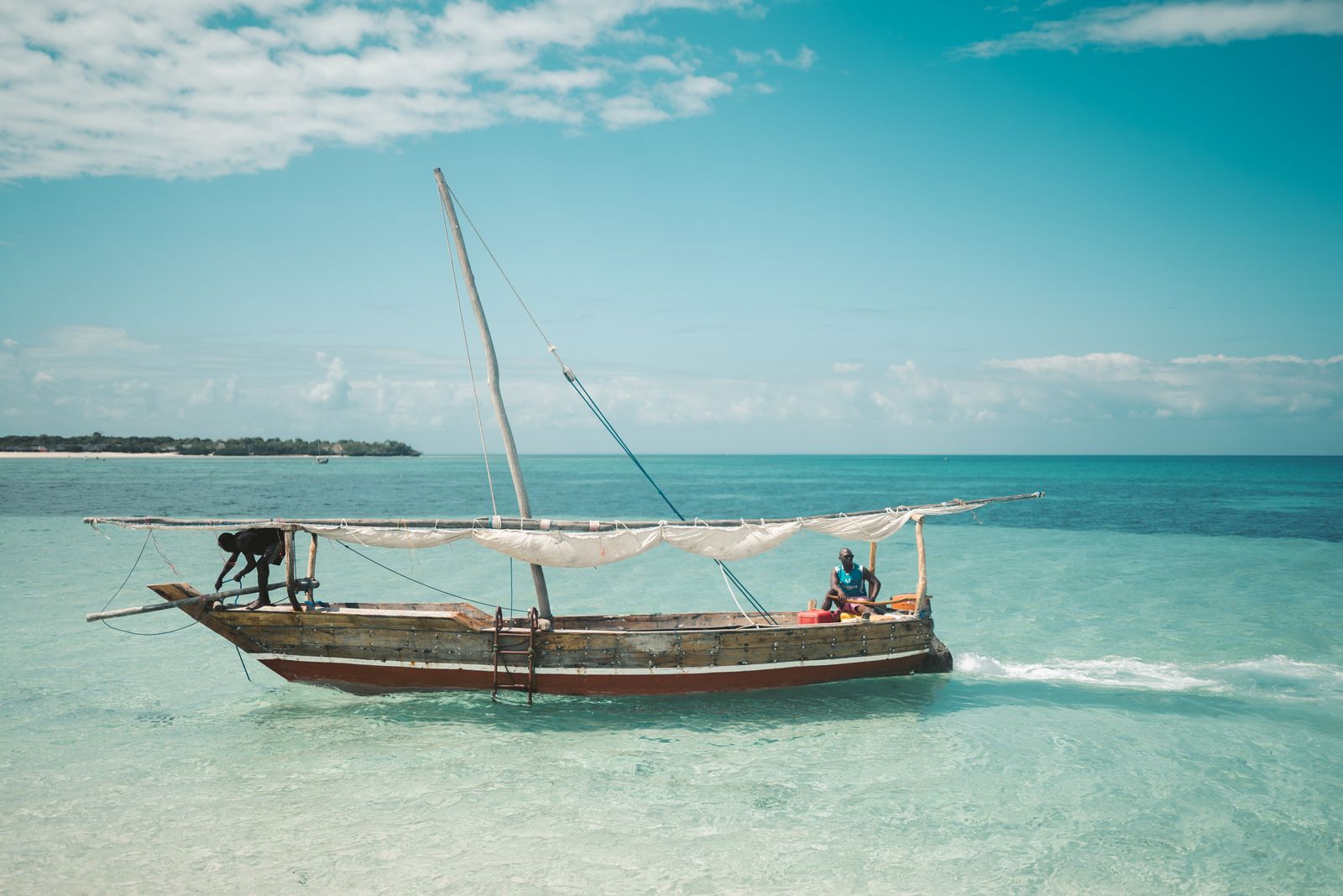 Boutre en bois à voile repliée sur l'eau turquoise de Zanzibar, deux pêcheurs à bord