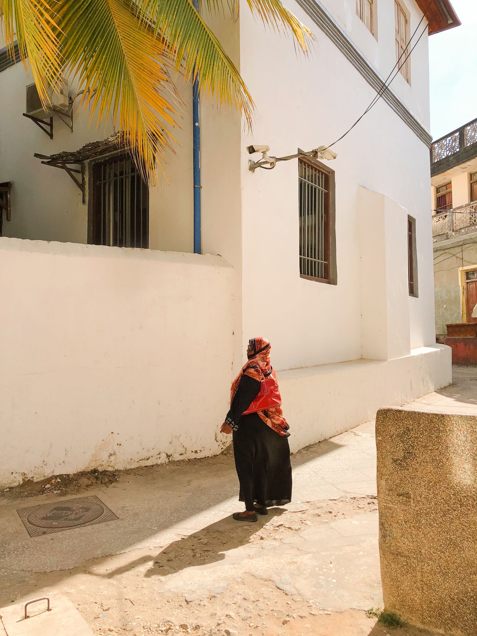 Femme en robe longue sombre et foulard rouge dans une ruelle blanche de Stone Town, à Zanzibar
