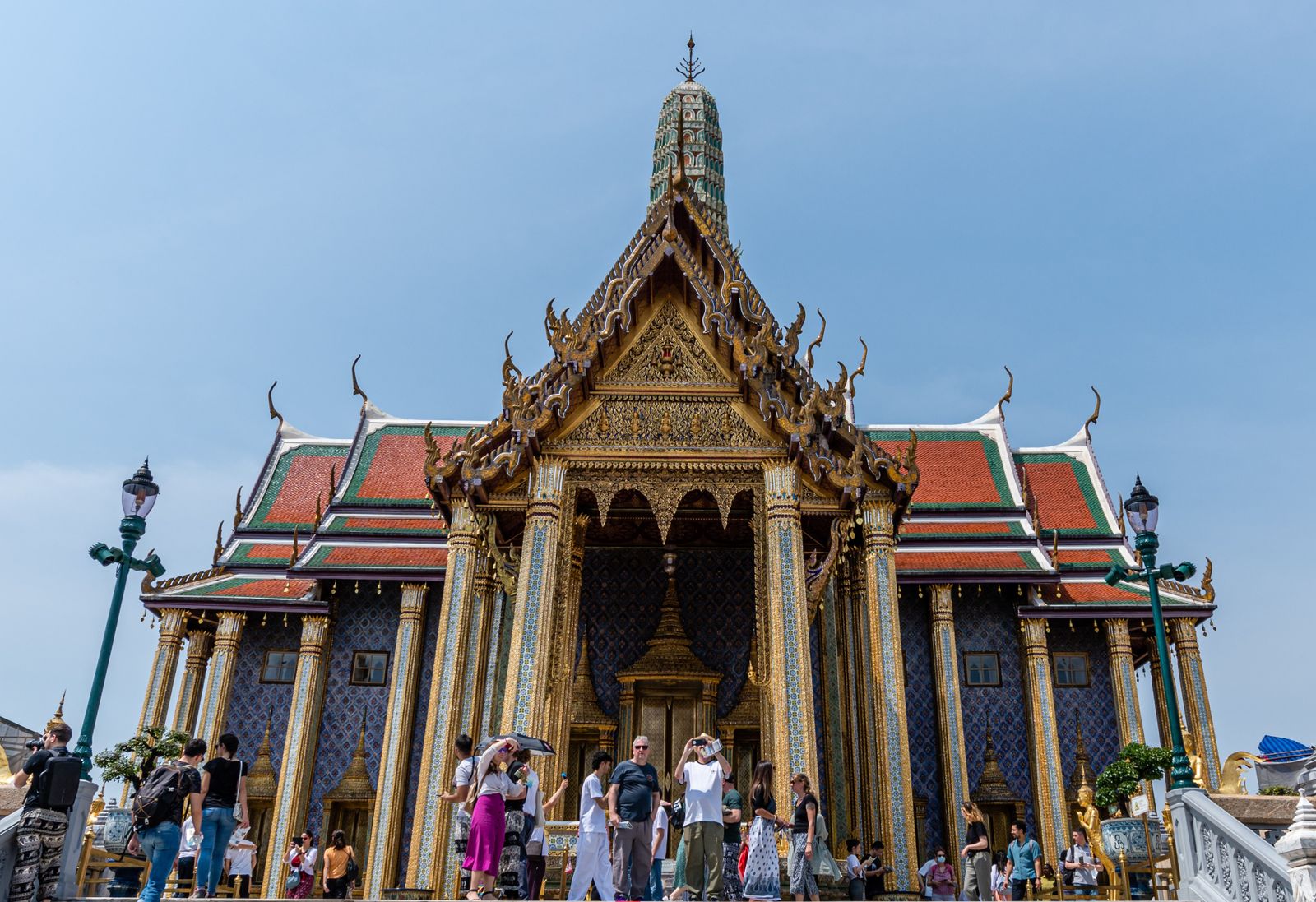 Temple richement décoré du Grand Palais de Bangkok, des visiteurs au pied des marches sous un ciel bleu