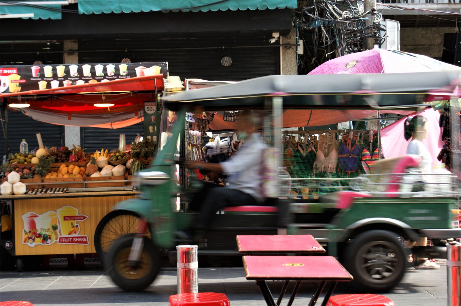 Tuk-tuk passant devant des étals de rue colorés à Bangkok
