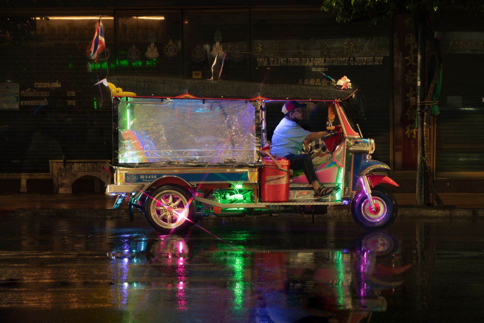 Tuk-tuk illuminé dans une rue de Bangkok sous la pluie, la nuit