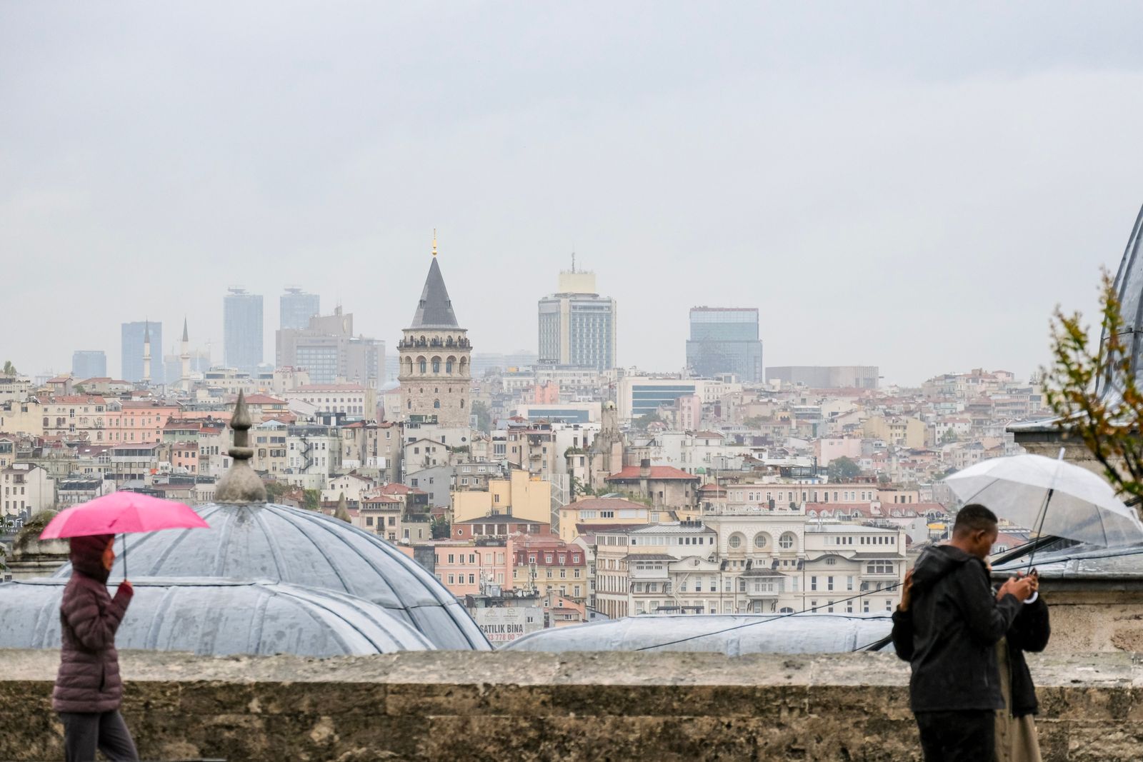 Deux passants sous des parapluies face à la tour de Galata, un jour de pluie à Istanbul