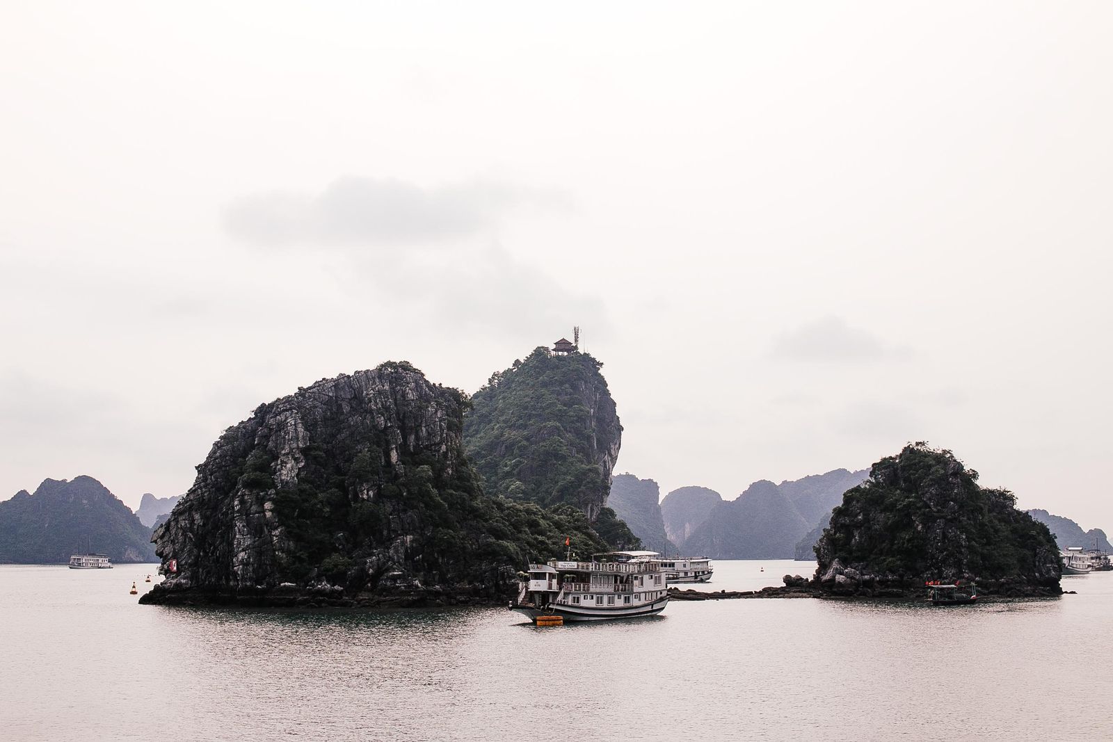 Pitons calcaires et bateaux de croisière dans la baie d'Ha Long, sous un ciel gris