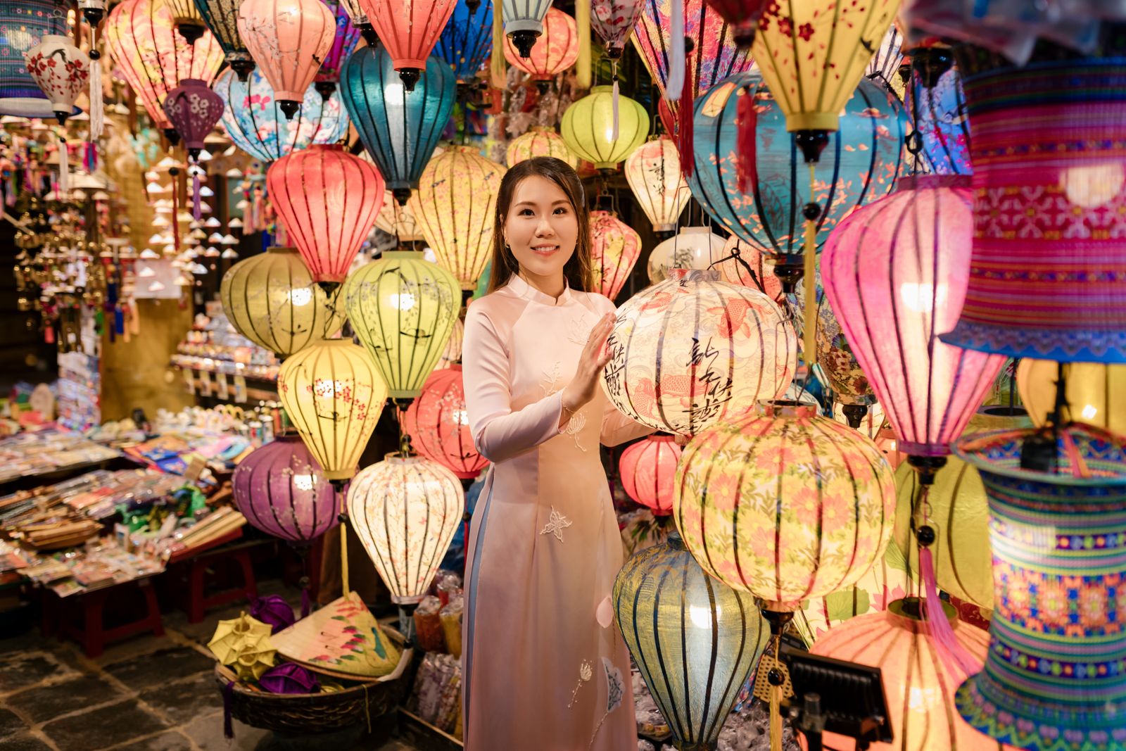 Femme en áo dài rose pâle au milieu des lanternes d'un marché de nuit à Hoi An